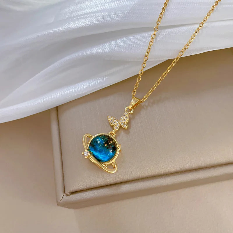 Unknown Product gold necklace with blue planet pendant and butterfly charm on beige surface