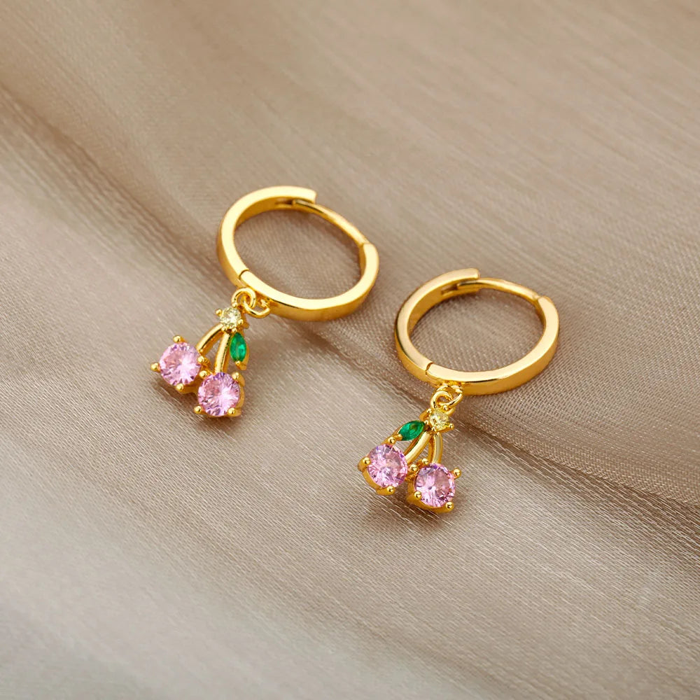 Gold hoop earrings with pink gemstones on a beige fabric background
