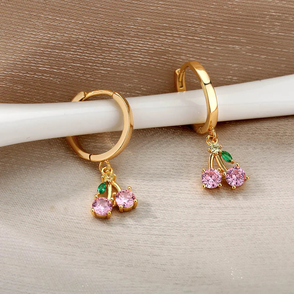 Gold hoop earrings with pink and green gemstones on a beige background