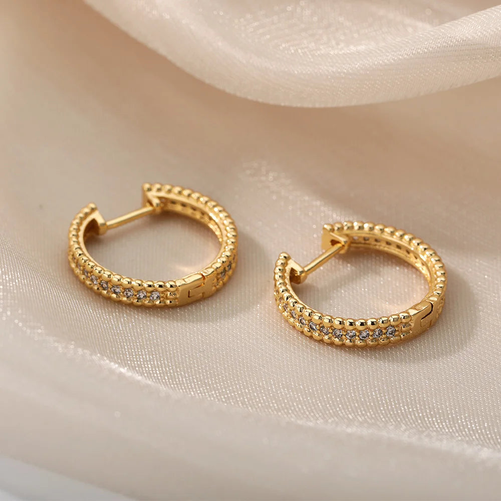 Gold hoop earrings with embedded stones on a beige fabric background