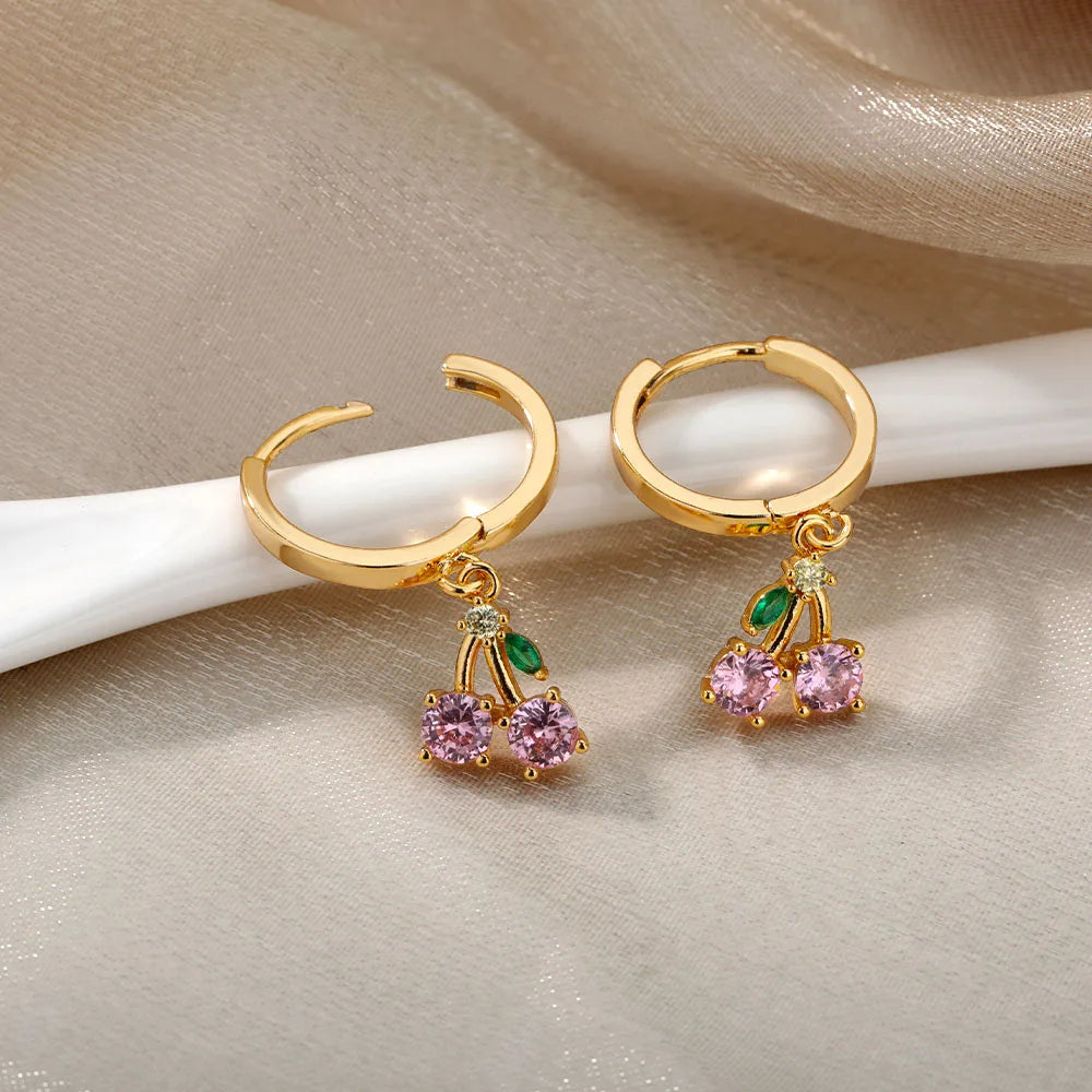 Gold hoop earrings with cherry-themed charms on a beige fabric background