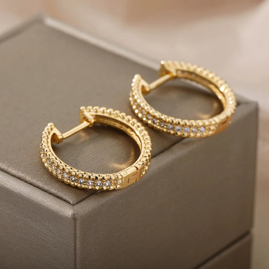 Gold hoop earrings with embedded stones on a gray box