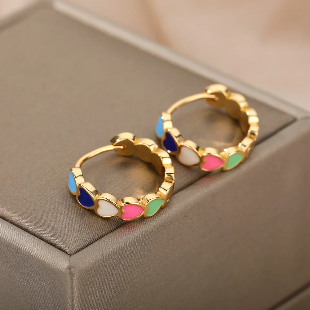 Gold hoop earrings with colorful heart-shaped stones on a gray surface