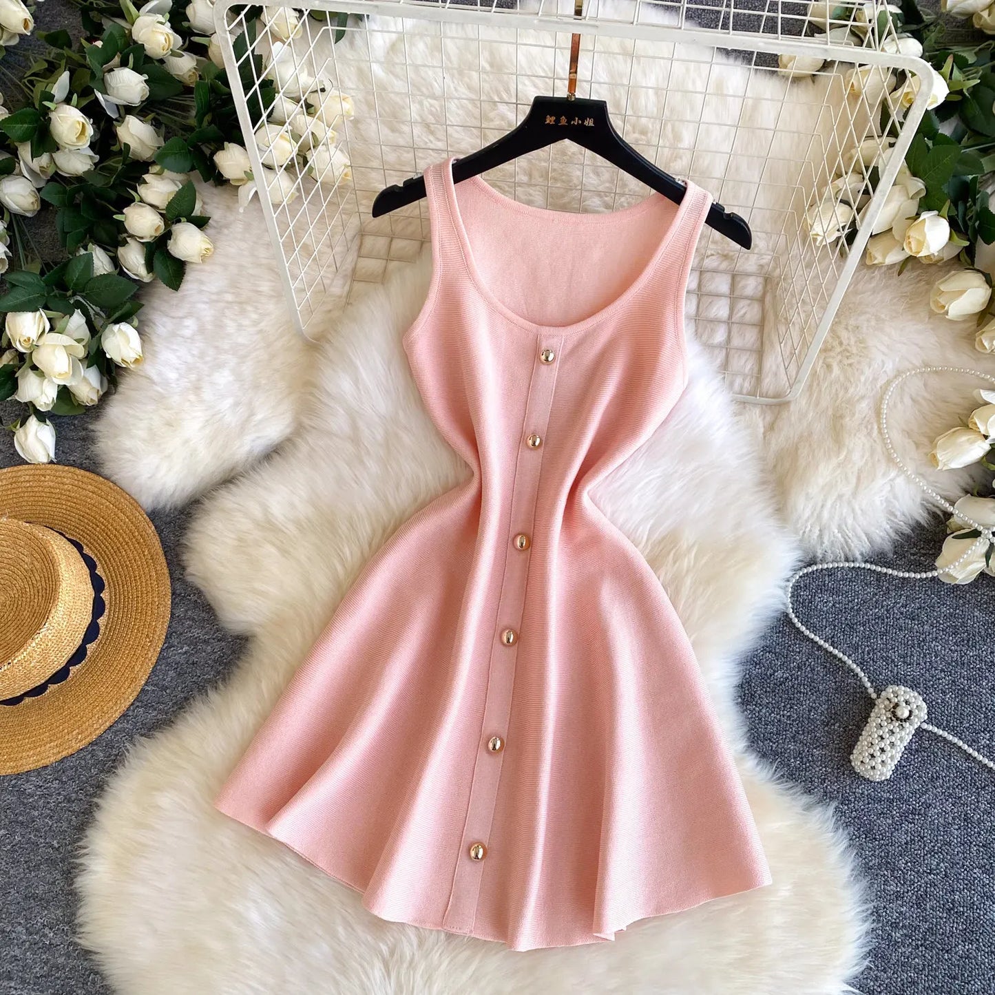 Pink dress with buttons on a hanger against a decorative background with flowers and a hat.