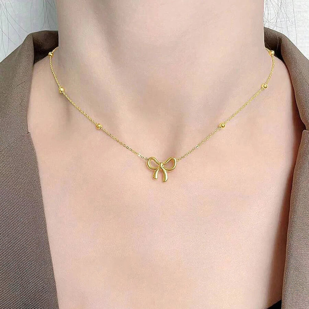 Gold necklace with a bow pendant on a person wearing a brown garment.