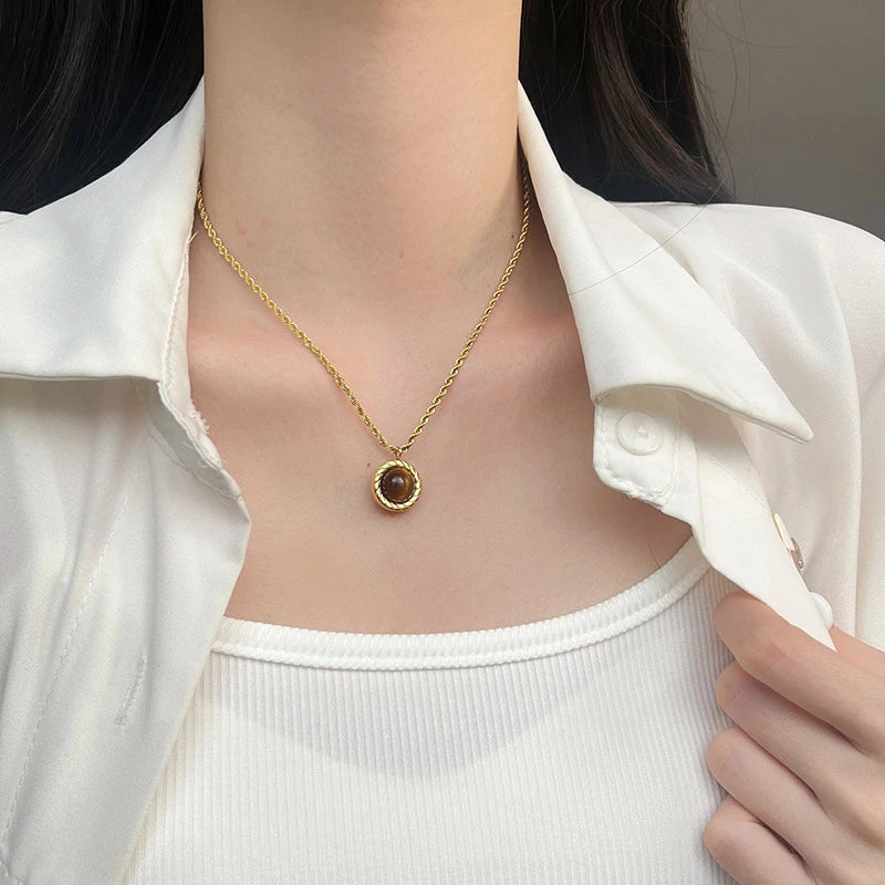 Gold necklace with a pendant worn by a person in a white shirt.