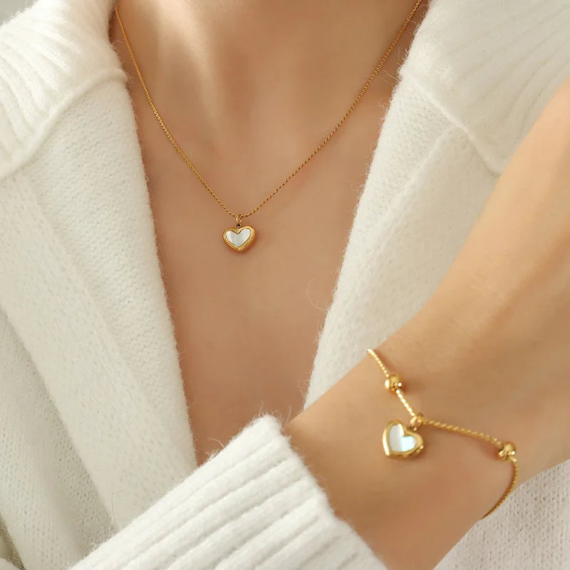 Gold heart necklace and bracelet on a person wearing a white sweater