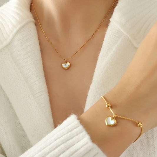 Gold heart necklace and bracelet on a person wearing a white sweater