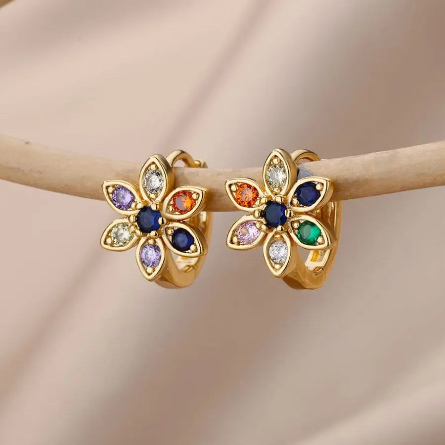 Gold flower-shaped earrings with multicolored gemstones on a beige background