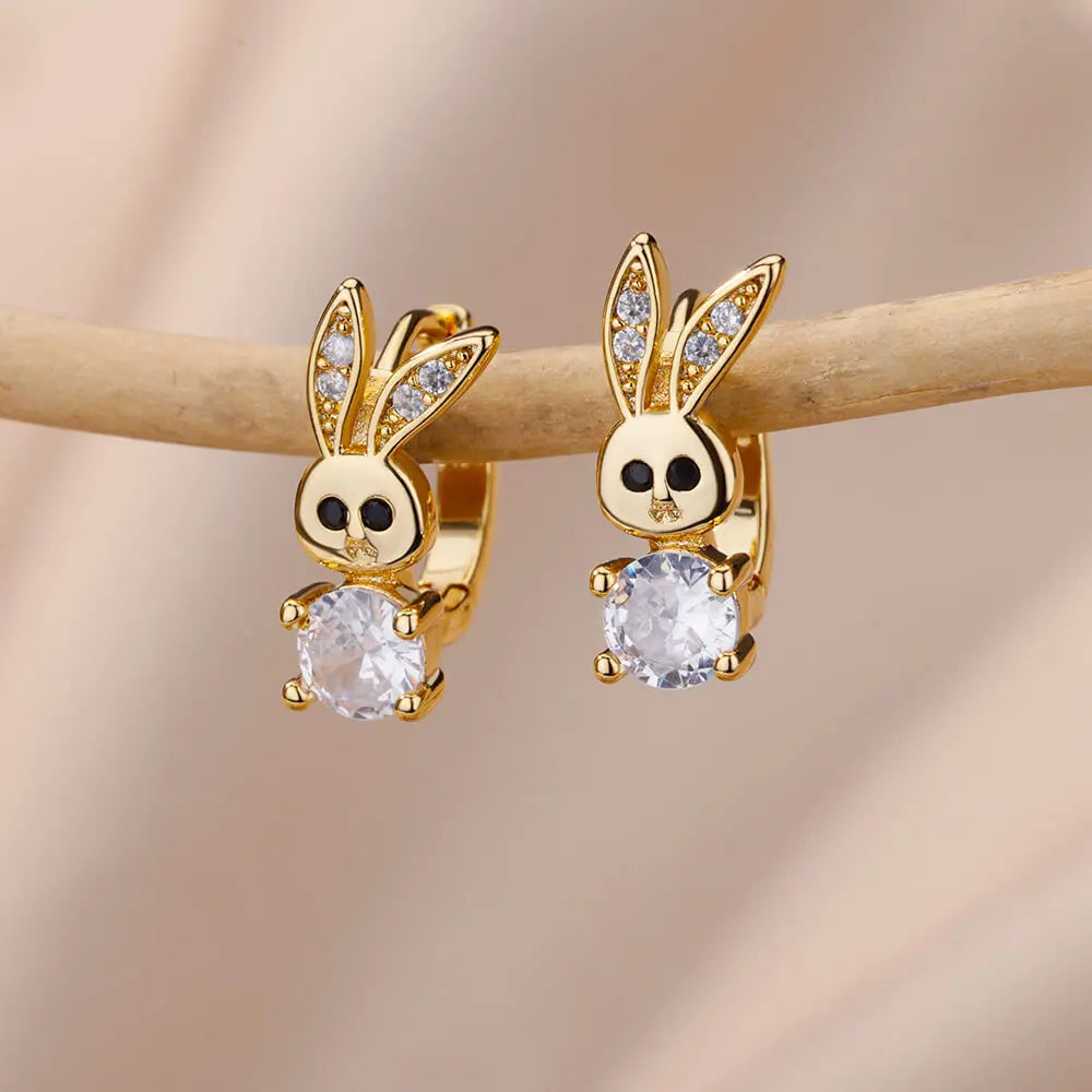 Gold bunny-shaped earrings with clear gemstones on a wooden stick against a beige background