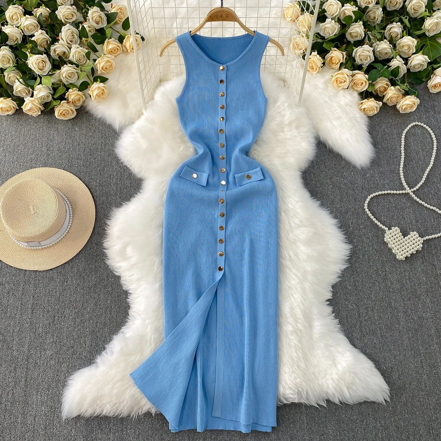 Blue dress on a hanger with decorative items like a hat, necklace, and flowers on a gray surface.