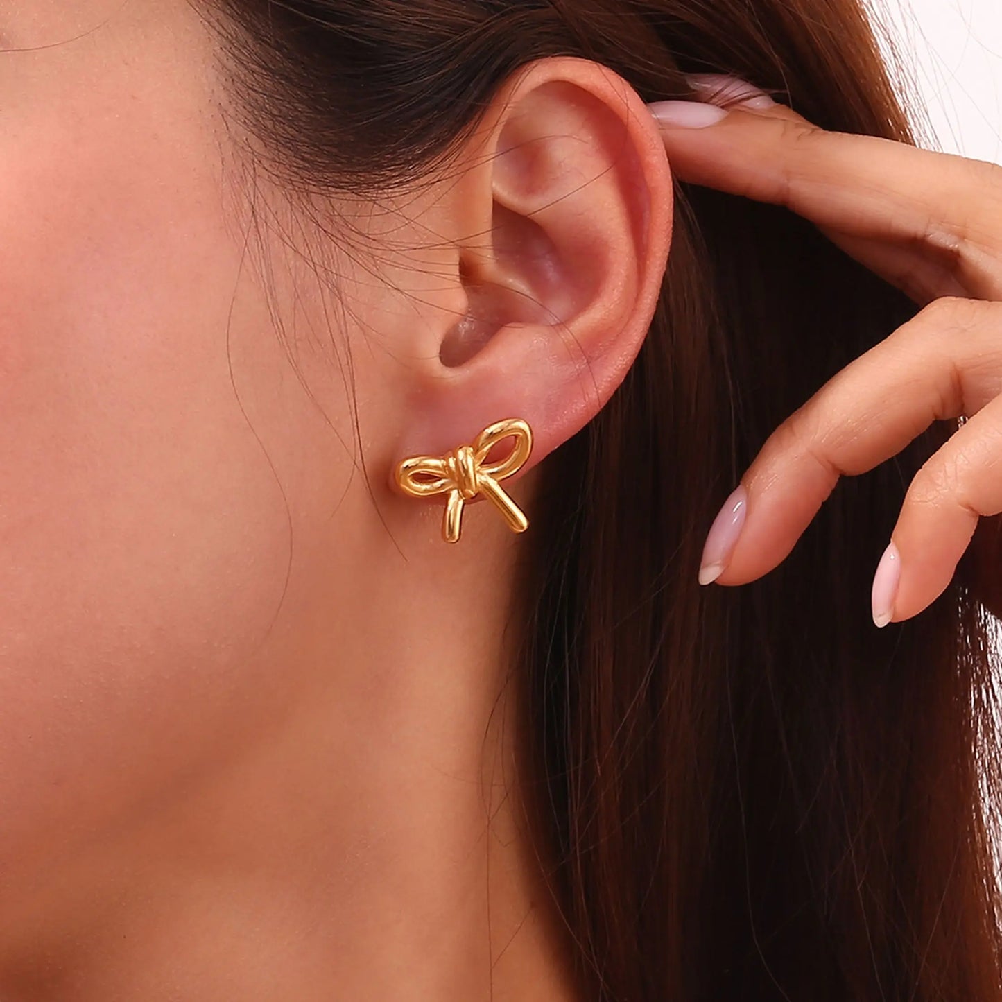 Gold bow-shaped earring worn by a person with a hand near their ear.