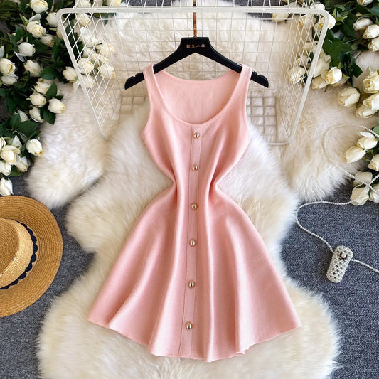 Pink sleeveless dress with buttons on a hanger against a decorative background with flowers and a hat.