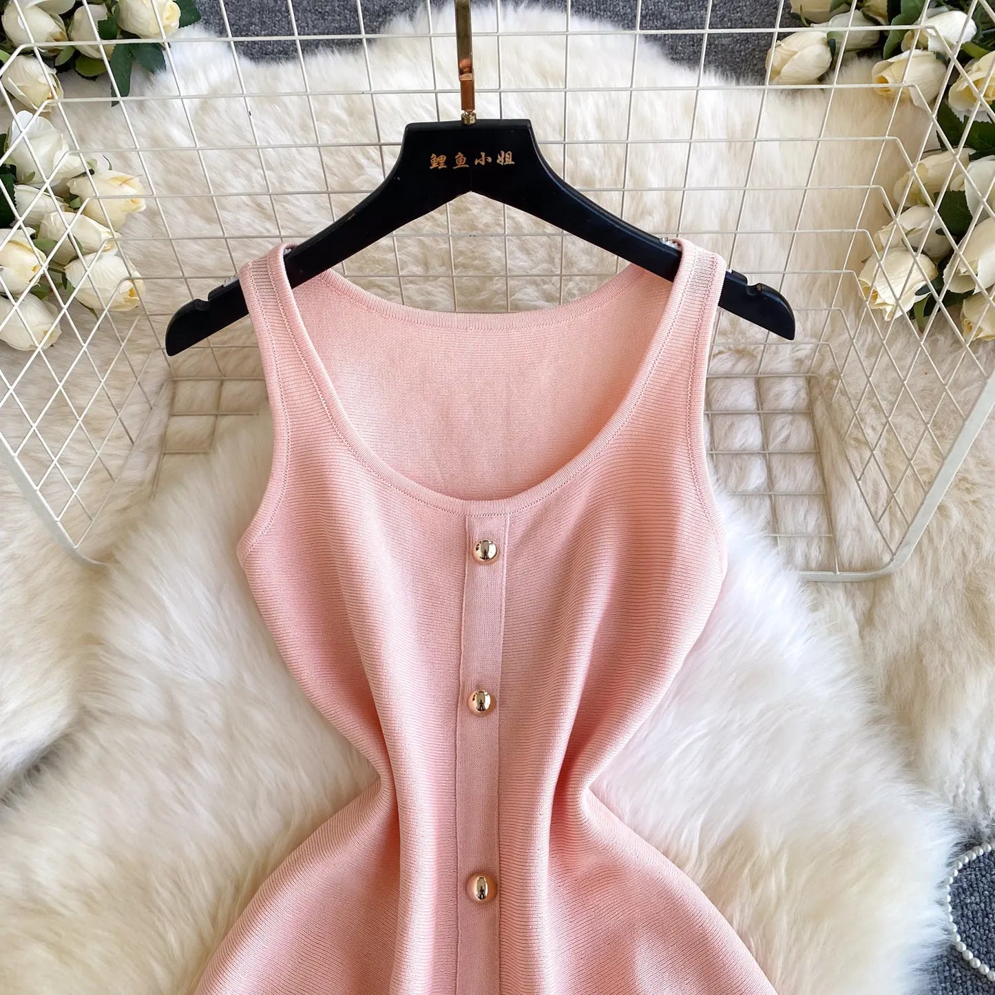 Pink sleeveless dress with gold buttons on a hanger against a white fur and floral background