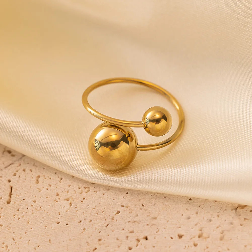 Gold ring with two spherical ends on a beige fabric background