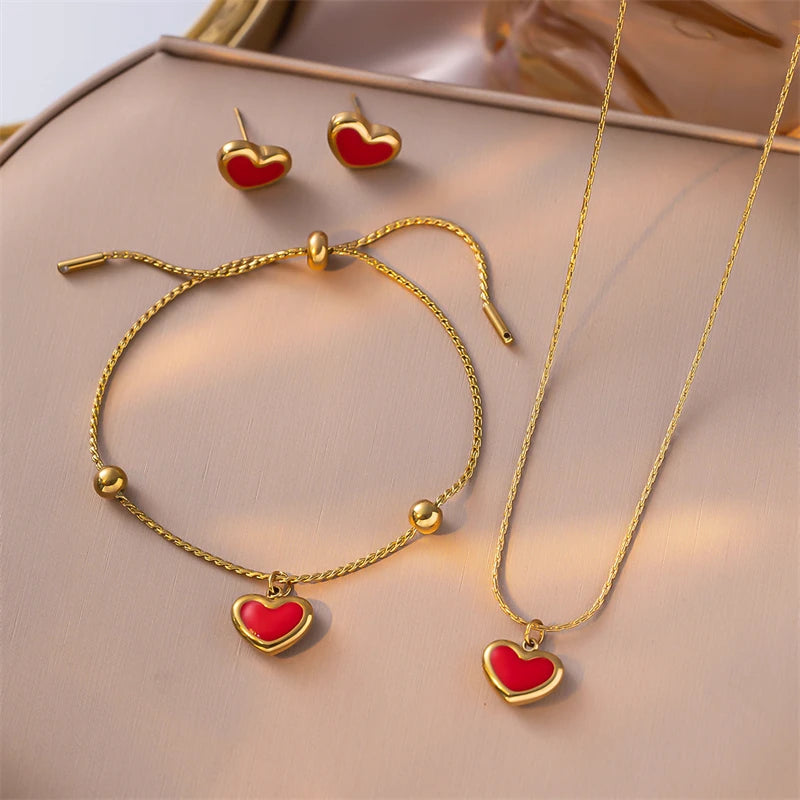 Gold jewelry set with red heart charms on a beige surface