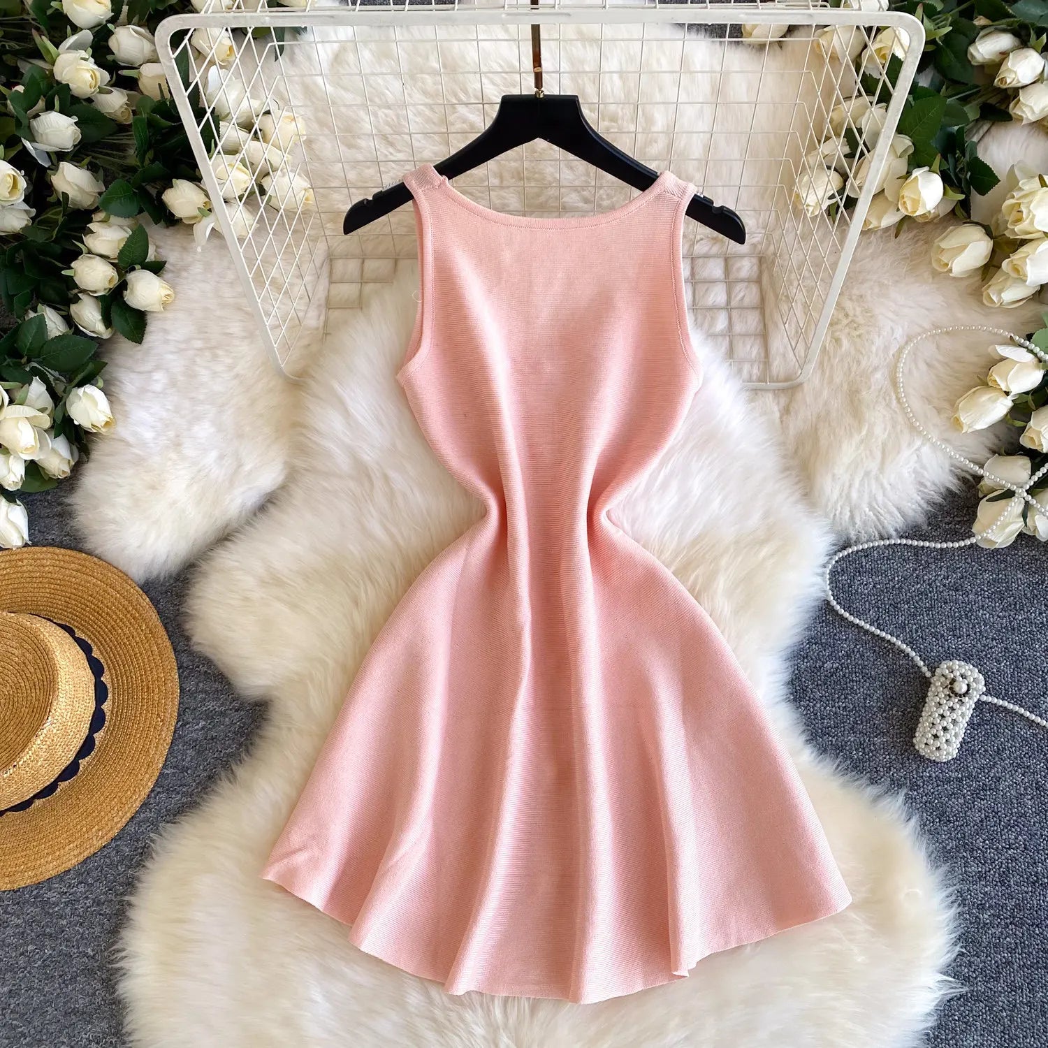 Pink dress on a hanger with floral decorations and a hat on a fur rug.