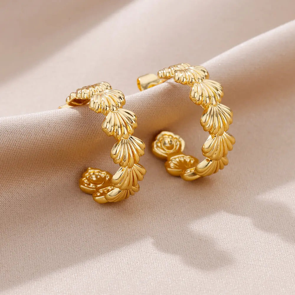 Gold hoop earrings with floral designs on a beige fabric background