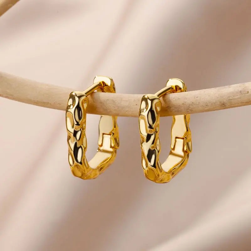 Gold hoop earrings on a wooden stick against a soft pink background