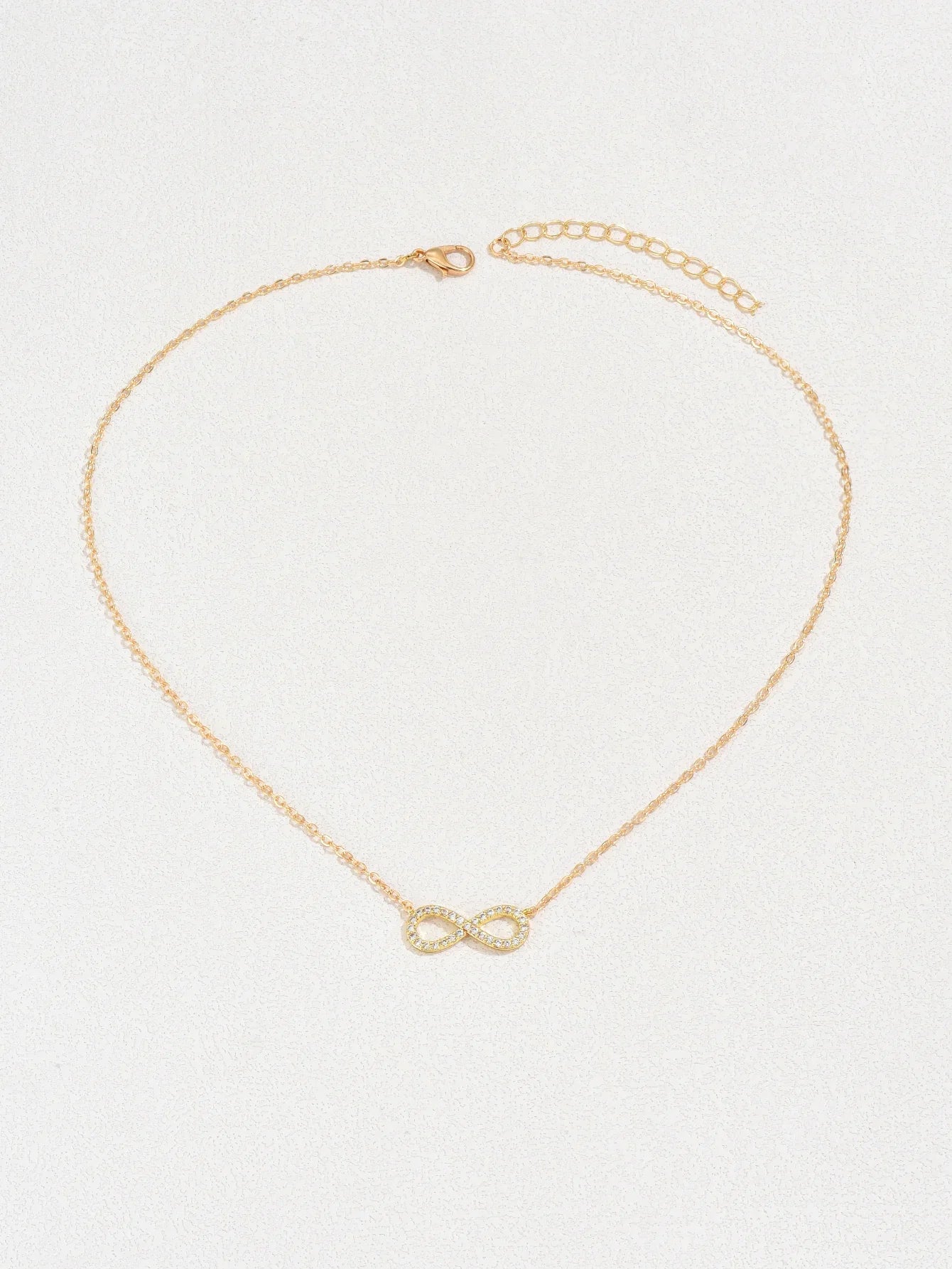 Gold infinity necklace on a light gray background