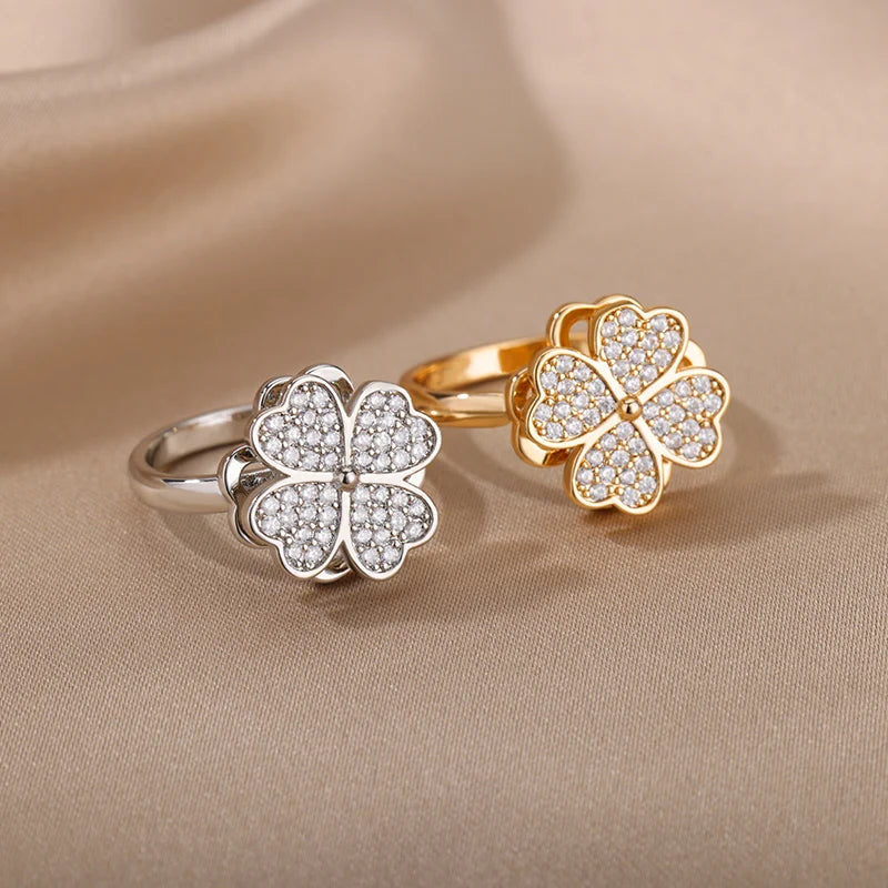 Two floral-shaped rings, one gold and one silver, on a beige fabric background.