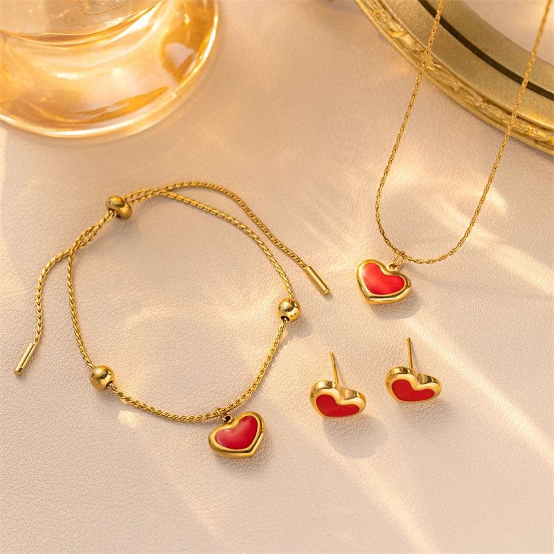 Gold jewelry set with red heart charms on a beige surface