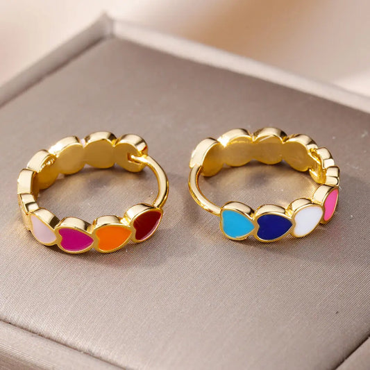 Pair of gold hoop earrings with colorful heart-shaped stones on a gray surface.